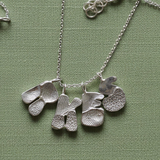 Silver necklace with leaf-shaped pendants held in a hand.